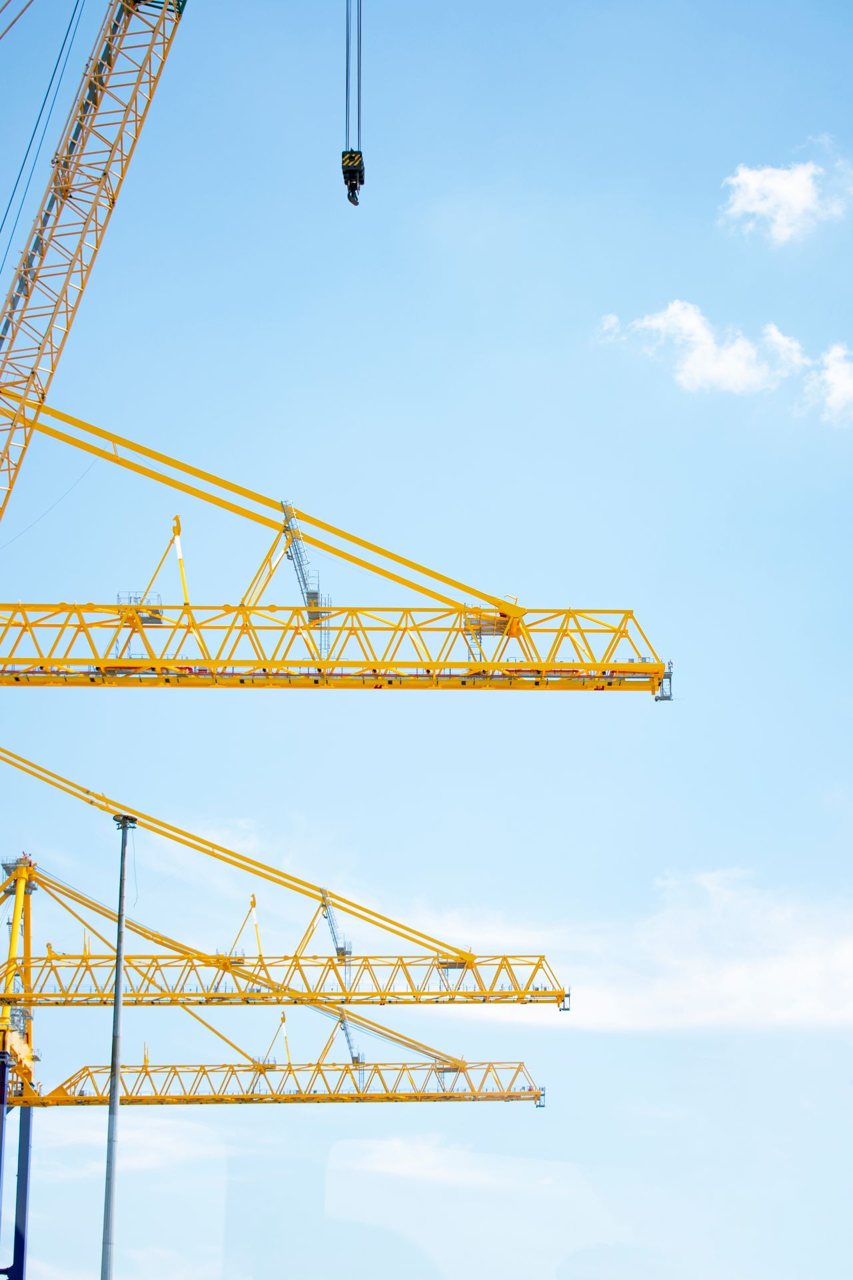 Free Yellow tower cranes in a construction site reaching into a clear blue sky, symbolizing modern industry. Stock Photo