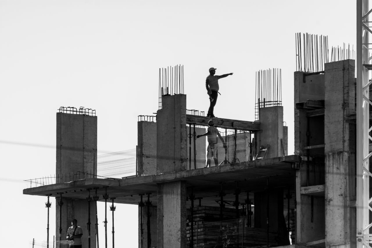 Free Silhouette of construction workers on a building site with one pointing towards the distance. Stock Photo