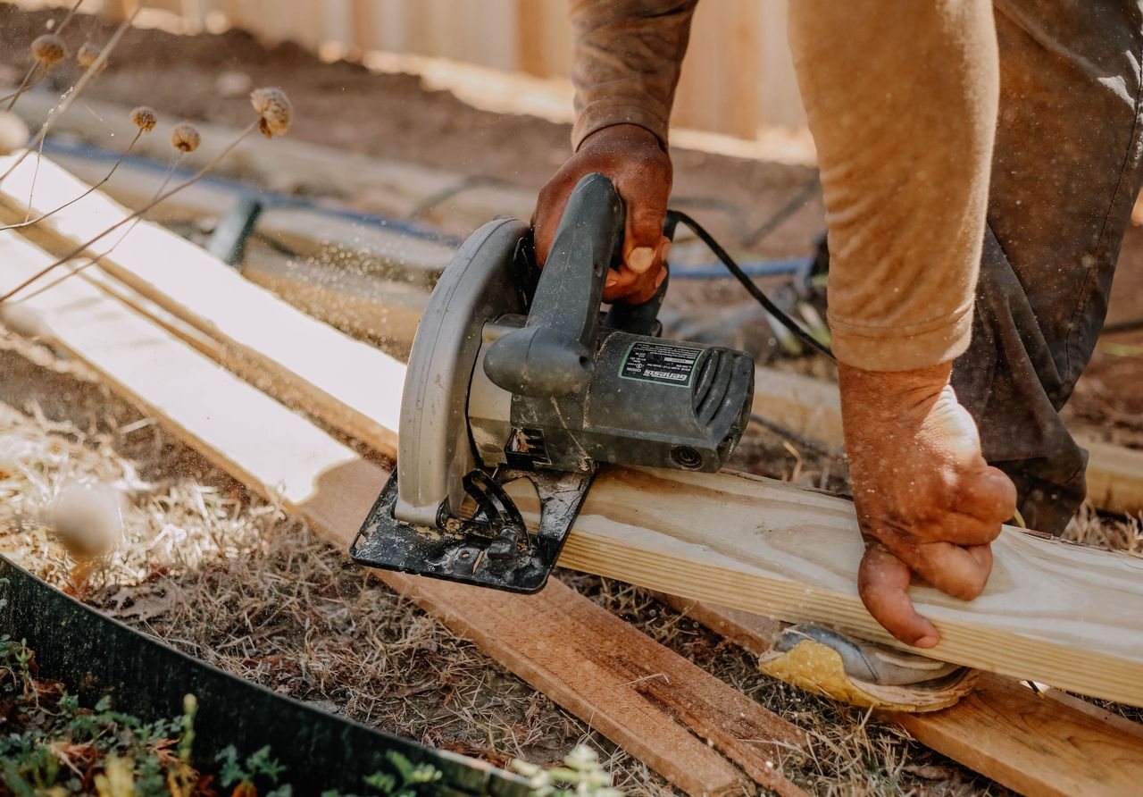Free Carpenter operating a circular saw on wooden planks outside, showcasing woodworking skills. Stock Photo